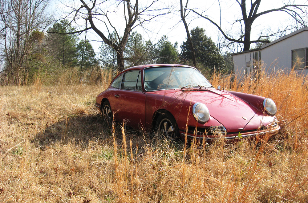 A red 911S sits alone in a field with tall grass.