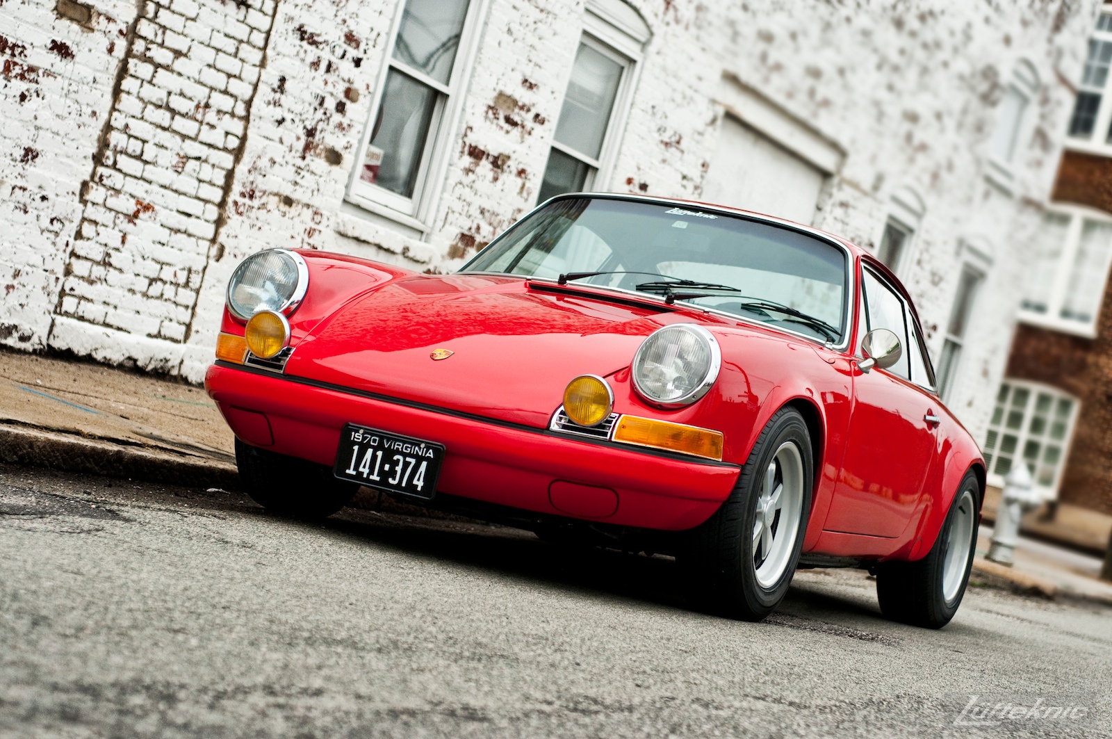 Bright red 1970 911E in front of a white wall.