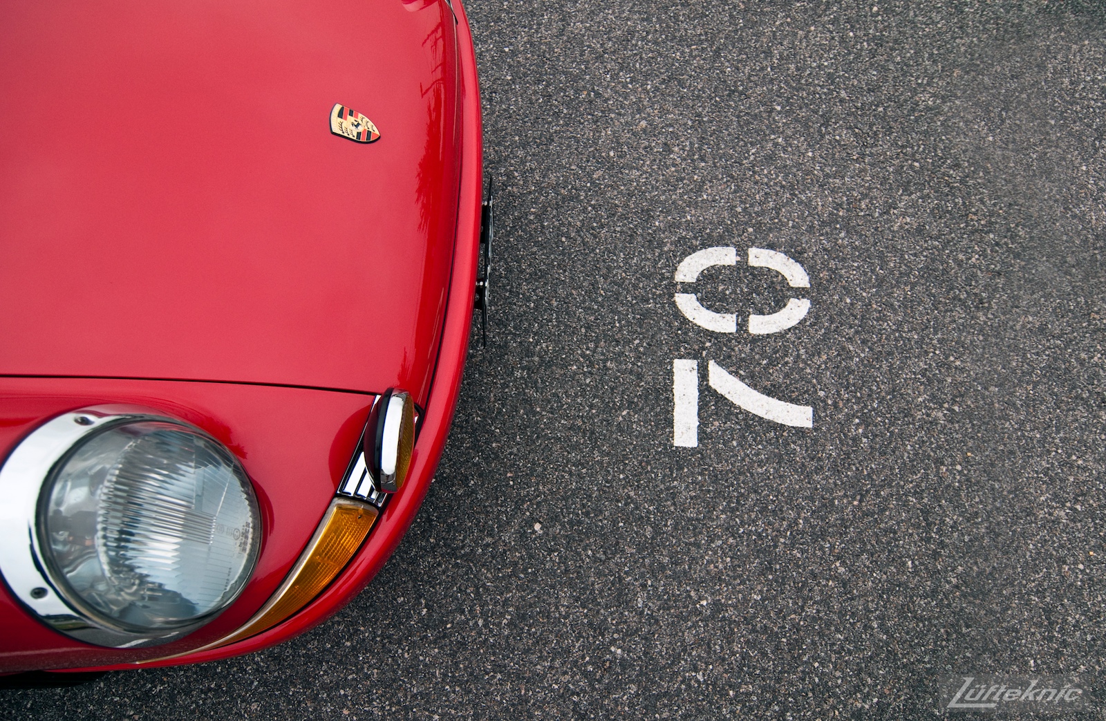 A red 1970 911E in a parking space marked 70.