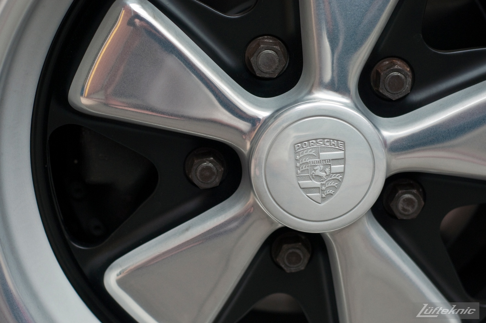 A close up picture of a Porsche center cap on a Fuchs wheel