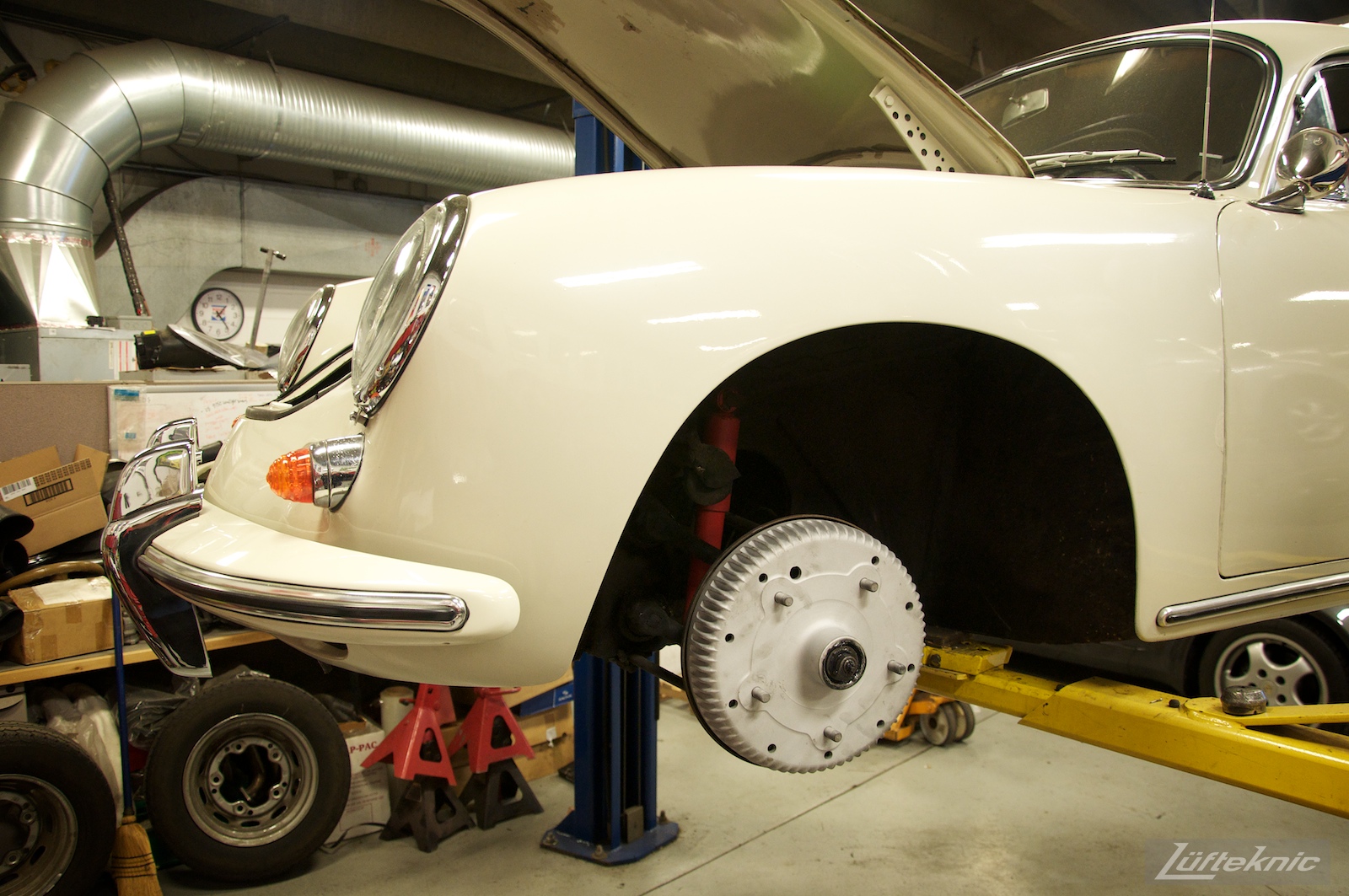 A white Porsche 356 on a lift at Lufteknic with the wheel removed showing a fresh brake drum