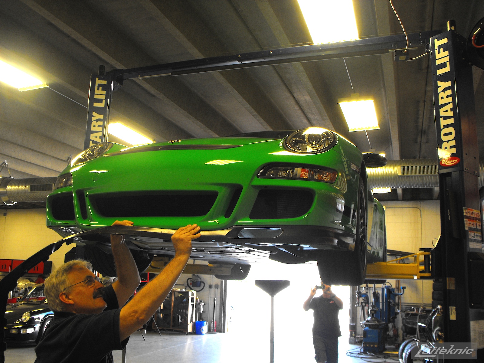 A Lufteknic employee removes the lower chin spoiler from a green Porsche 997.1 GT3 RS.