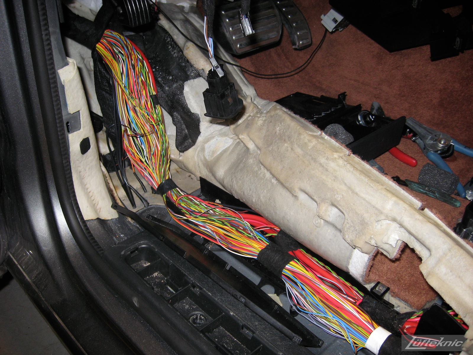 The carpet pulled aside with a large bundle of exposed wires inside the cabin of a Porsche Cayenne.