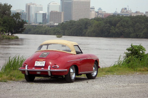 A red Porsche roadster pictured from the rear next to a lake.