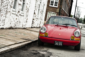 A red 911E parking near a white brick building with atmosphere.