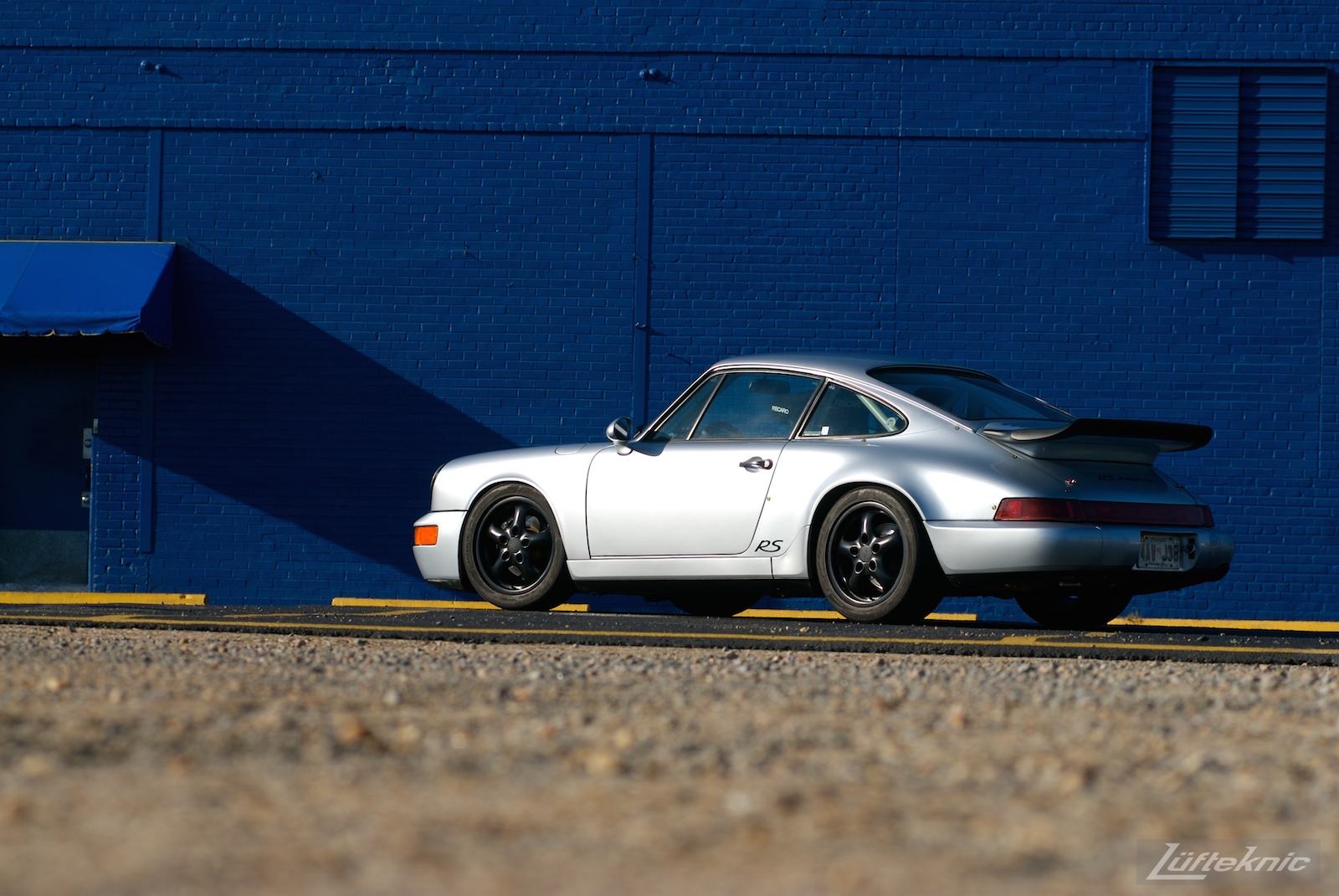 A Big blue wall with a beautiful silver Porsche 911 RS America