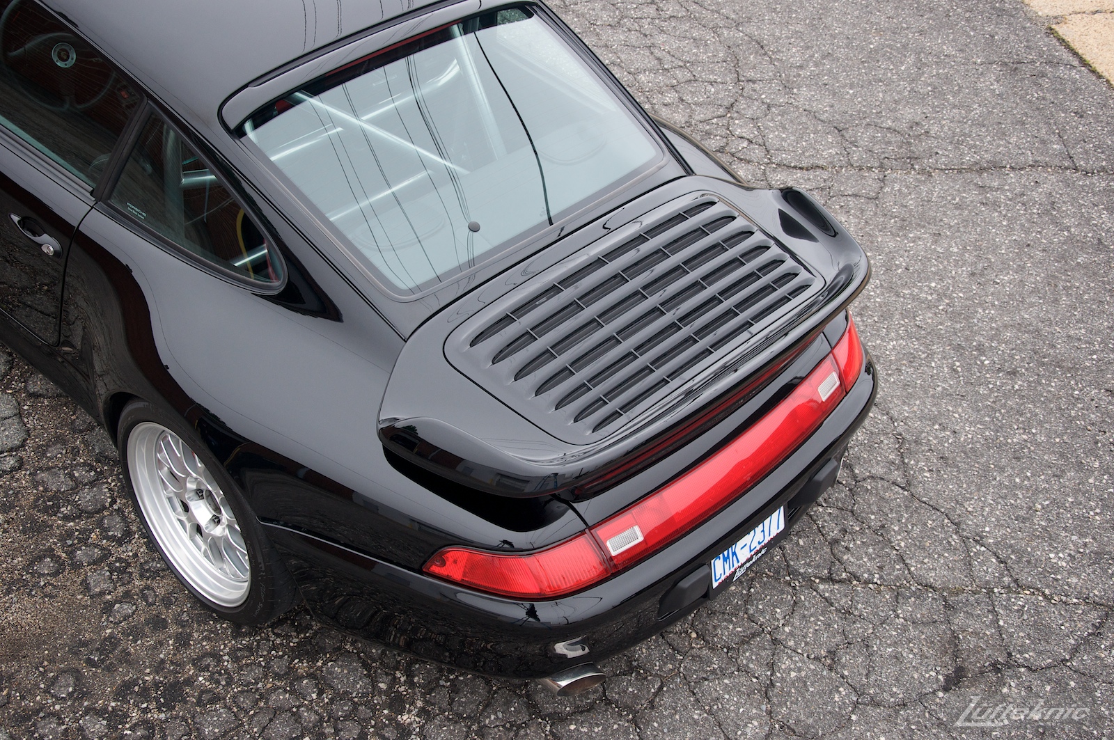 A view from above and behind a shiny black 993 Porsche Turbo in a parking lot showing rear lights and spoiler.