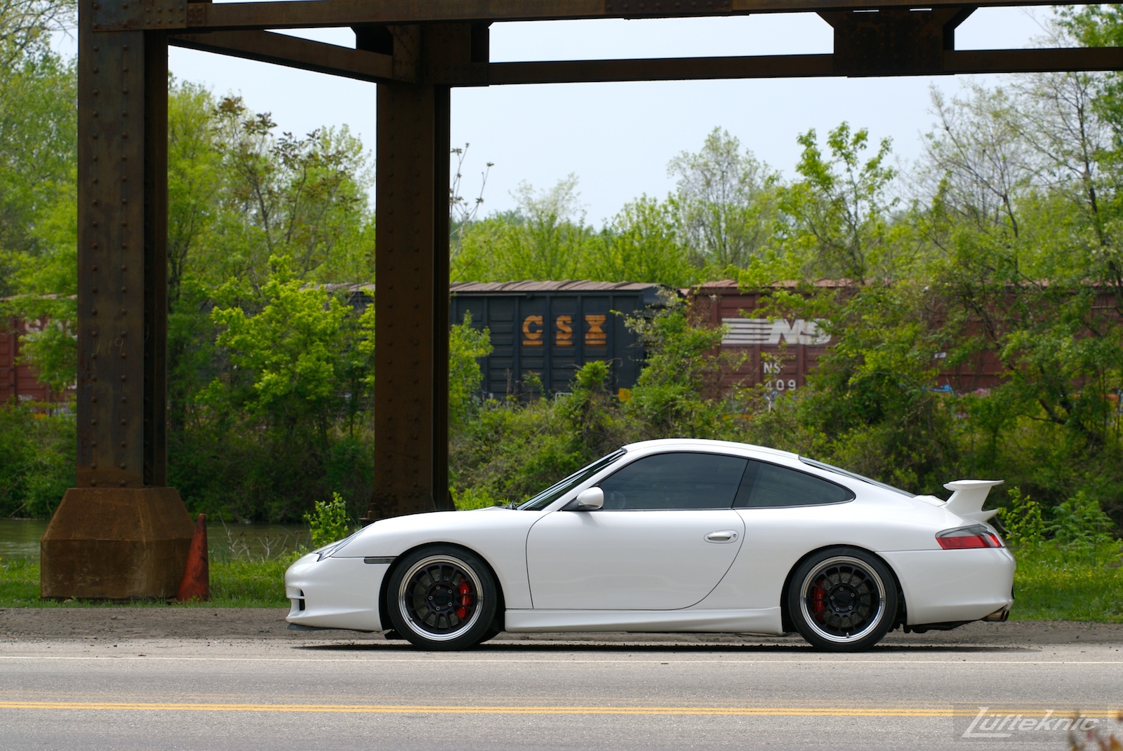 A track-prepped white Porsche 996 Gt3 with Fikse wheels in front of a train.