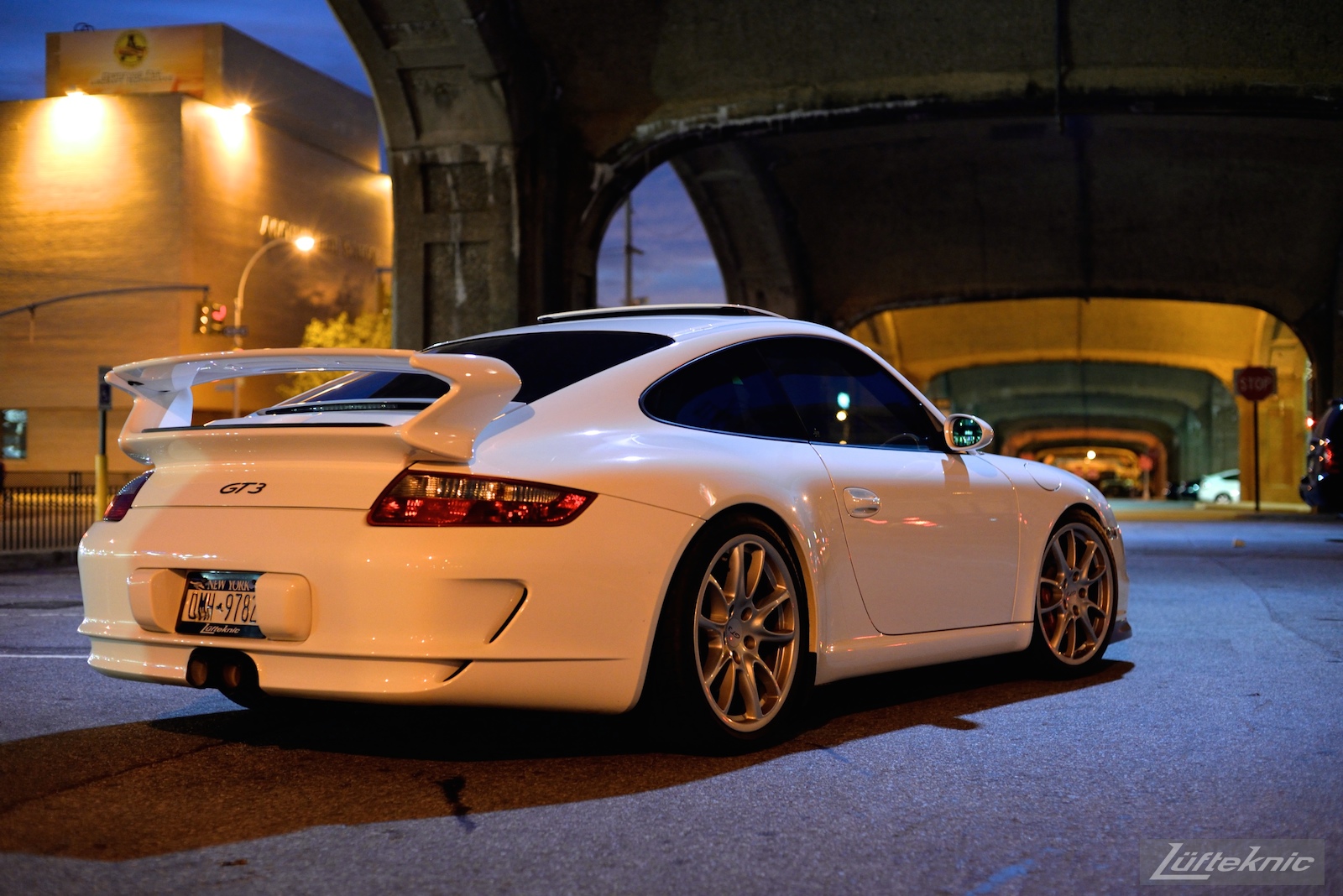 A white 997 GT3 viewed from behind under the 7 train bridge on Queens blvd at night.