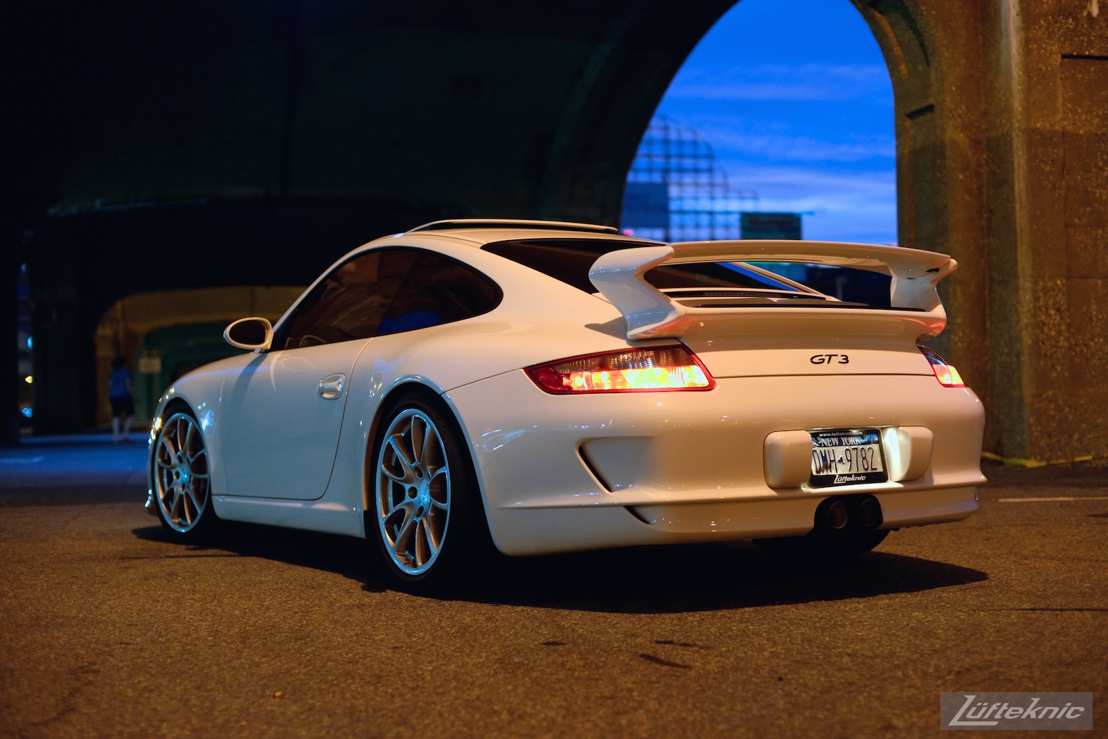 A white 997 GT3 viewed from behind under the 7 train bridge on Queens blvd at night.