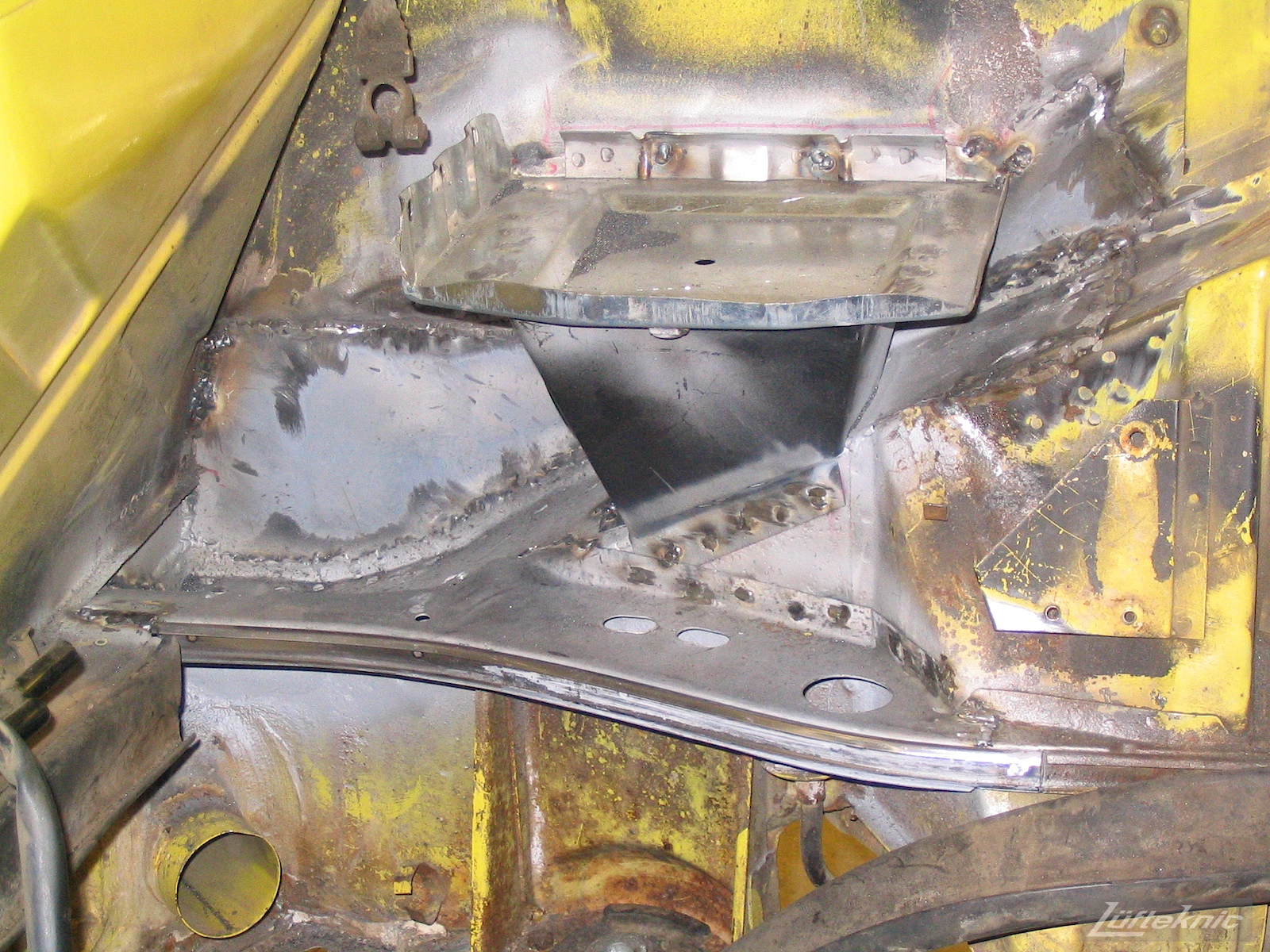 A picture showing repair of significant rust damage on the chassis of a yellow Porsche 914.