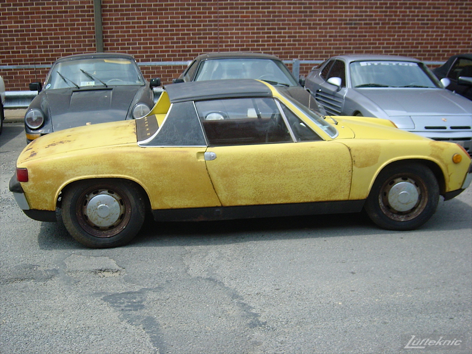 An old rusty 914 sitting in a parking lot with other Porsches before restoration.