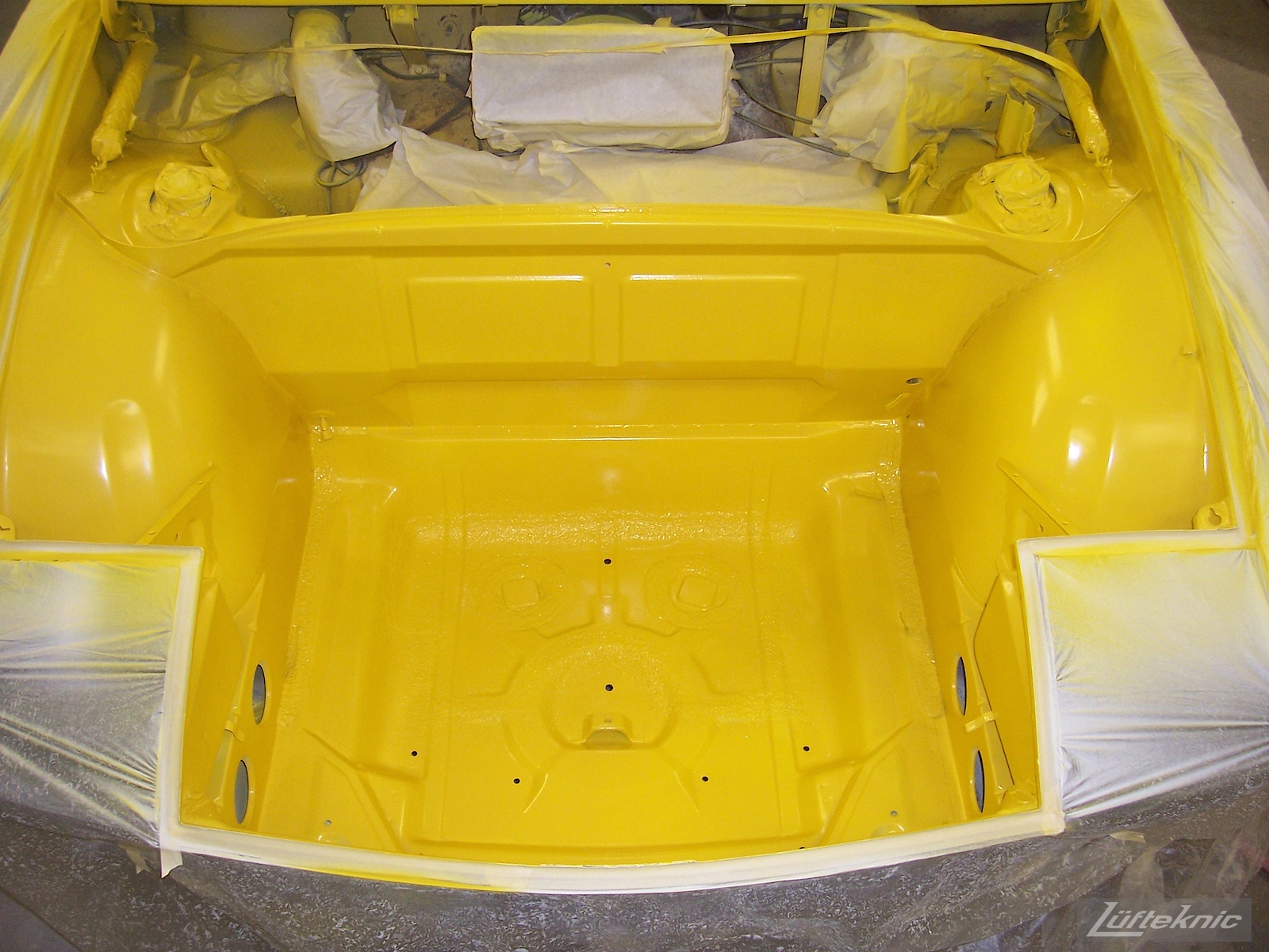Fresh yellow paint in the front trunk of a Porsche 914 being restored.