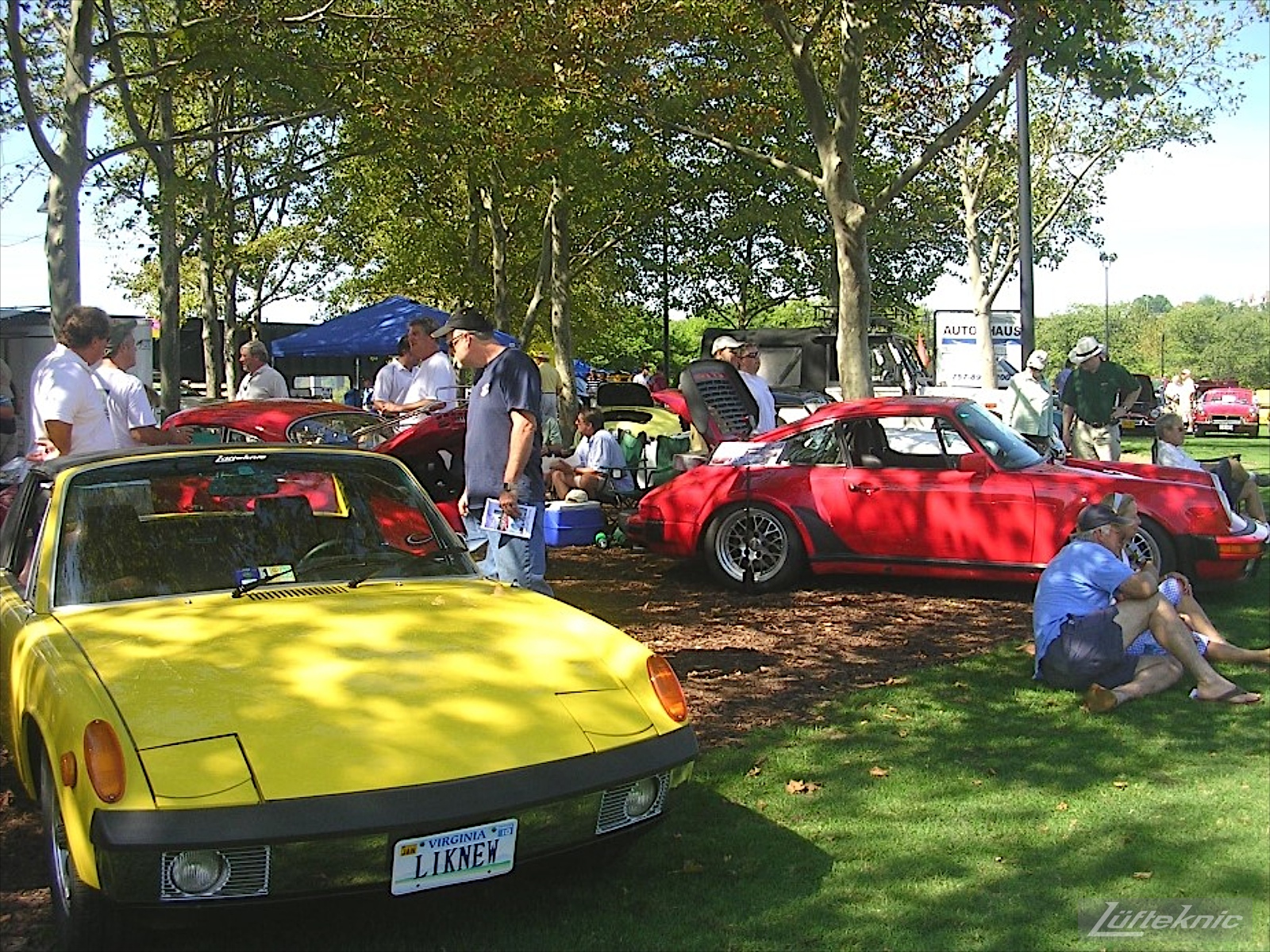 A restored yellow Porsche 914 on display with other Porsches at a car show.