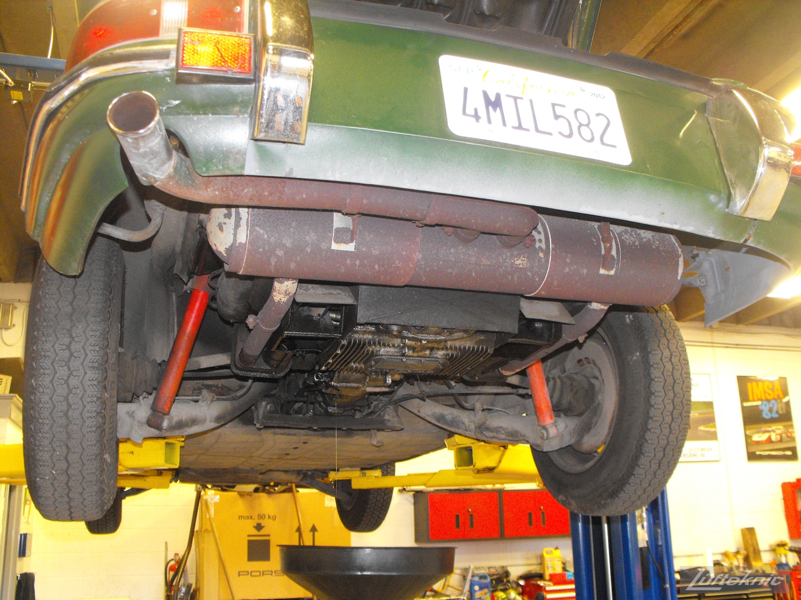 A rusty muffler exposed and oily bottom of the engine of an Irish Green Porsche 912 undergoing restoration at Lufteknic.